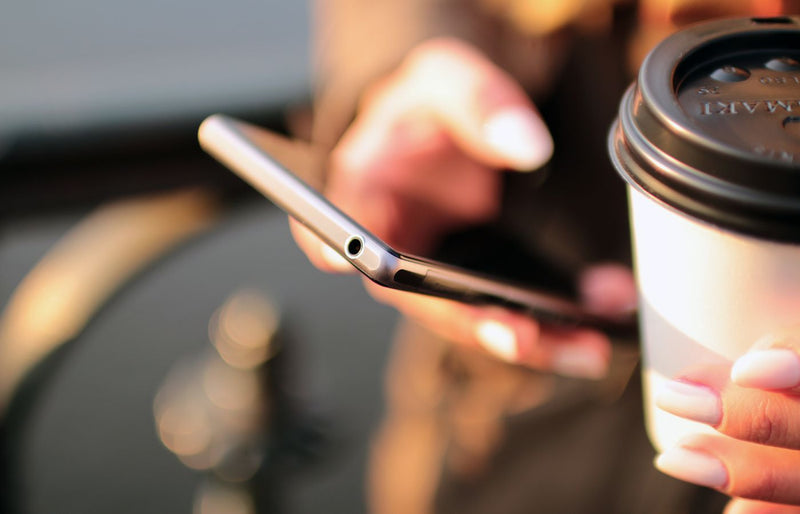 Person holding a smartphone and a takeaway coffee cup while texting outdoors.