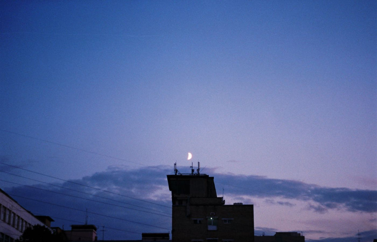 Tranquil crescent moon in evening sky above city buildings, serene dusk time.