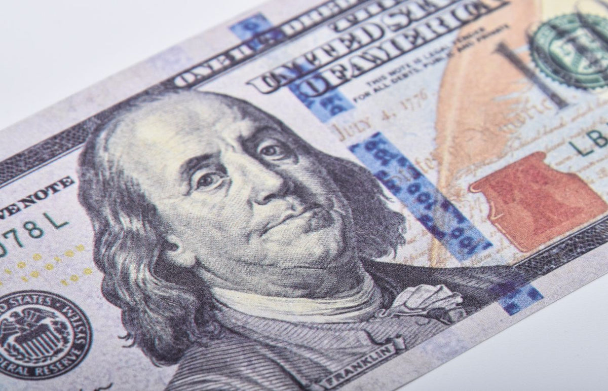 Macro shot of a US hundred dollar bill featuring Benjamin Franklin on a white surface.