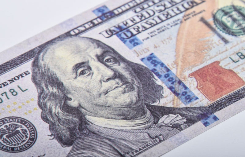 Macro shot of a US hundred dollar bill featuring Benjamin Franklin on a white surface.