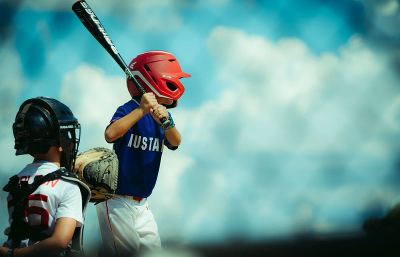 Young baseball players during a game, featuring a batter and a catcher in protective gear.
