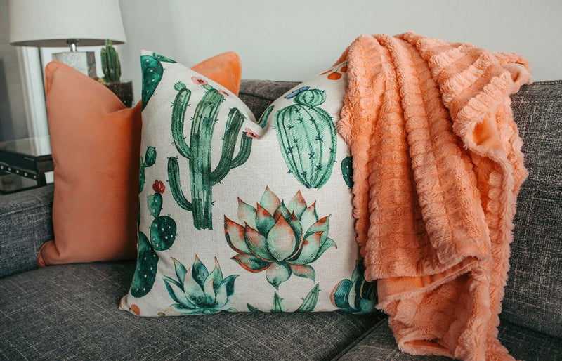 Elegant interior decor featuring cactus-themed pillows and a cozy blanket on a modern couch.