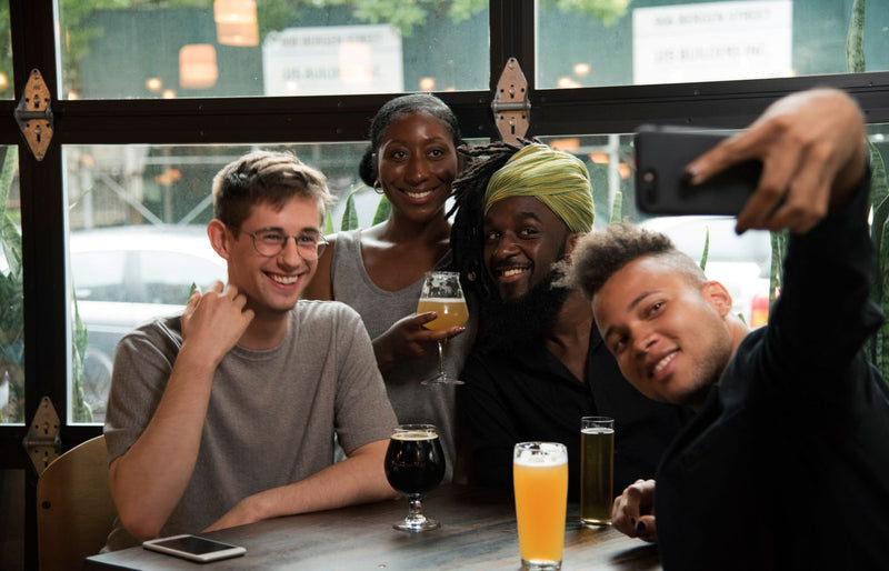 Group of cheerful friends taking a selfie, enjoying drinks at a bar.
