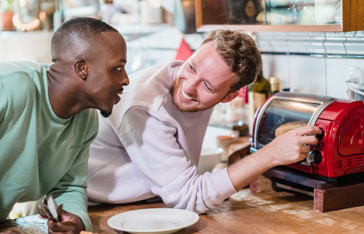 Two men sharing a joyful morning in a kitchen, preparing breakfast with smiles.