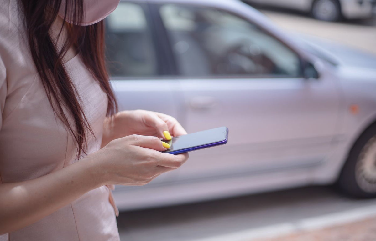 A close-up of a woman texting on a smartphone near a parked car outdoors.