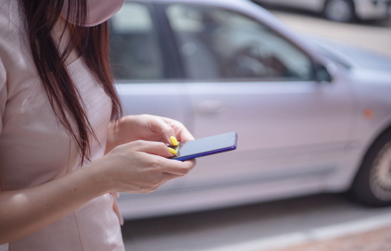 A close-up of a woman texting on a smartphone near a parked car outdoors.
