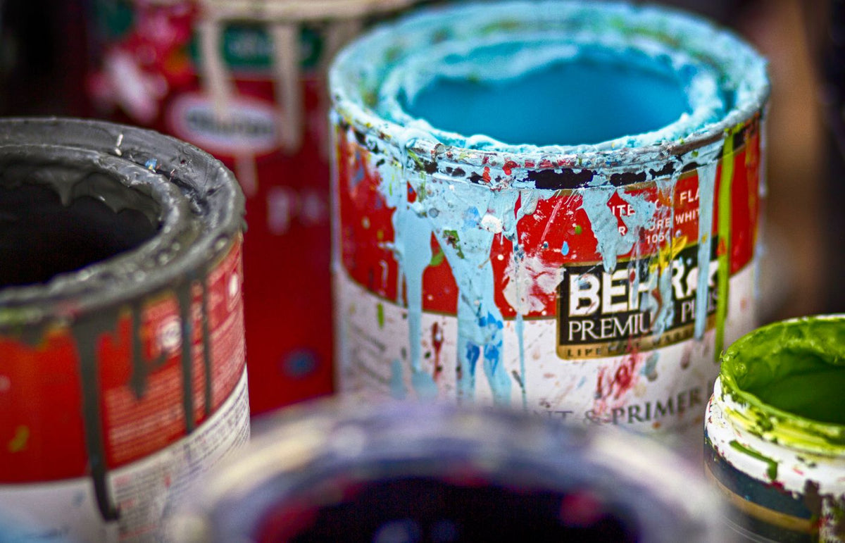 Close-up of vibrant, messy open paint cans with colorful splatters on a workshop surface.