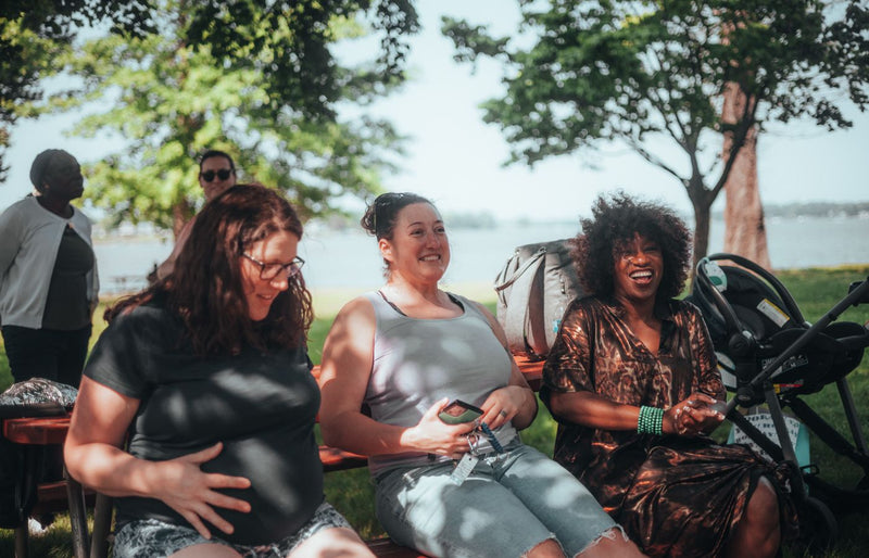 Group of diverse women sitting outdoors, sharing joyful moments in a sunny park setting.