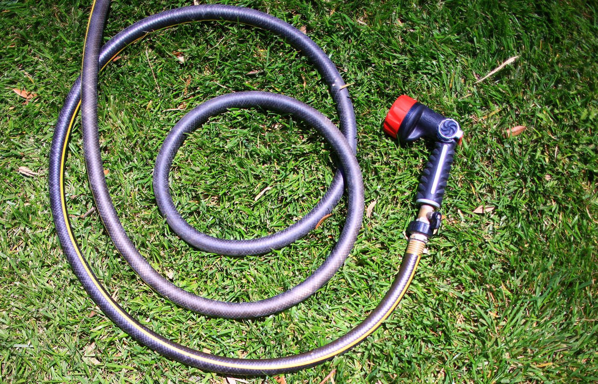 Curled garden hose on lush green grass, shot from above in bright daylight.