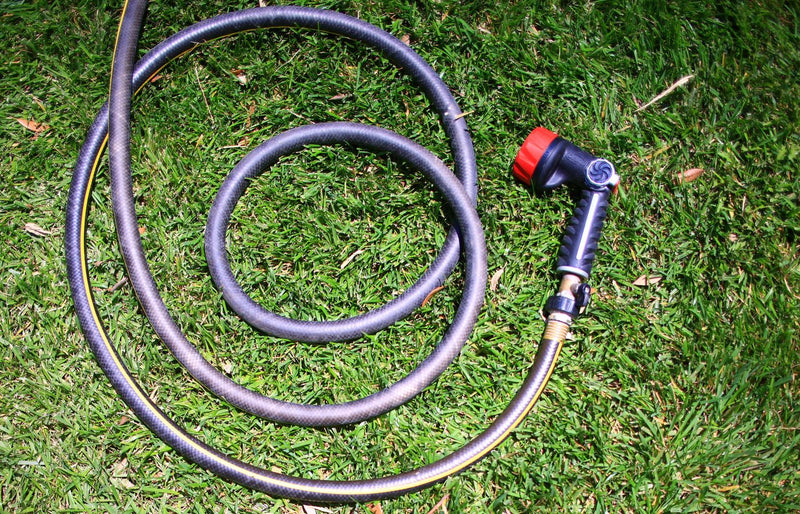 Curled garden hose on lush green grass, shot from above in bright daylight.