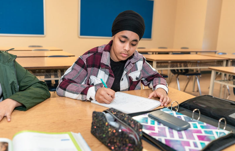 Teenage student writing at a desk in a classroom, focusing on learning and education.