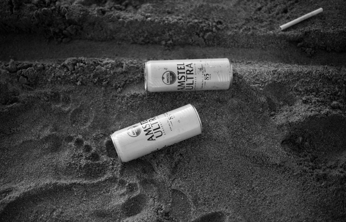 Black and white image of beer cans littered on the beach sand.