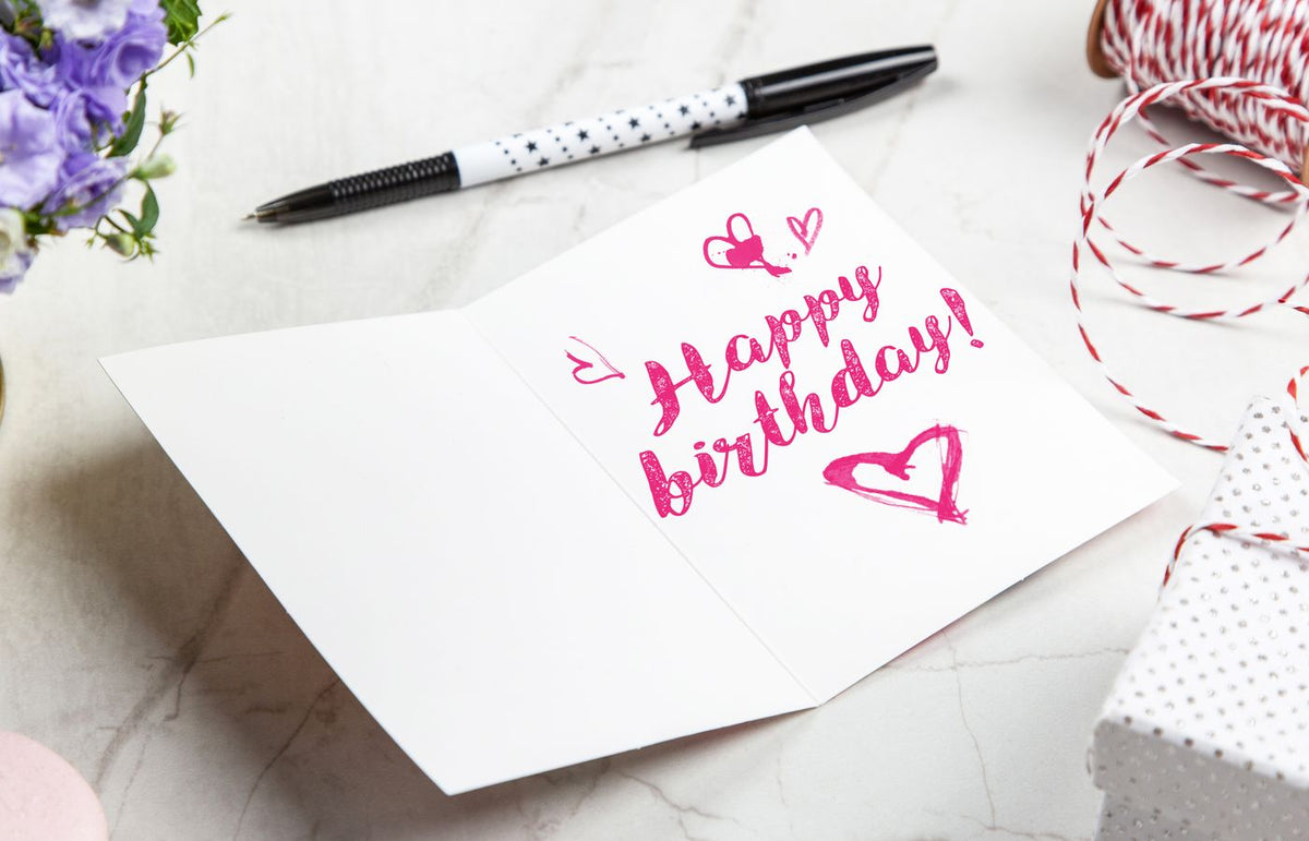 A vibrant birthday card with heart illustrations, surrounded by a pen, flowers, and gift wrap.