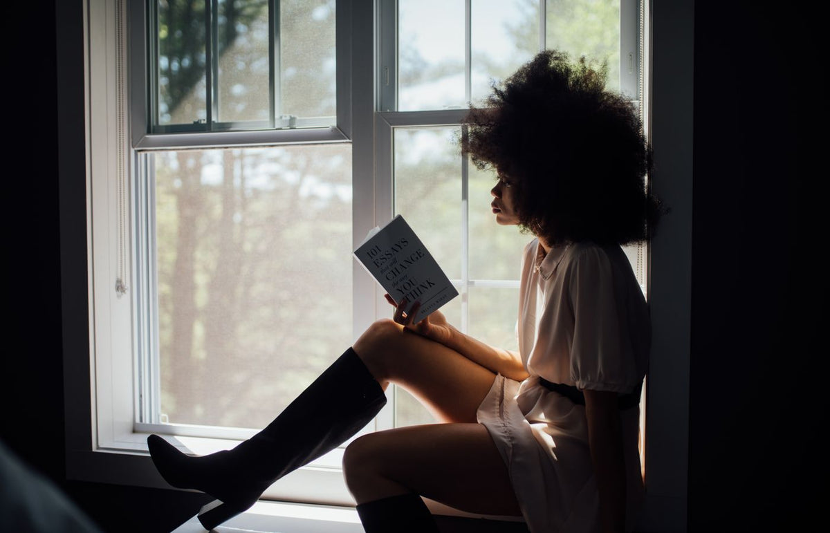 A woman enjoys a peaceful reading session by a window, bathed in natural light.