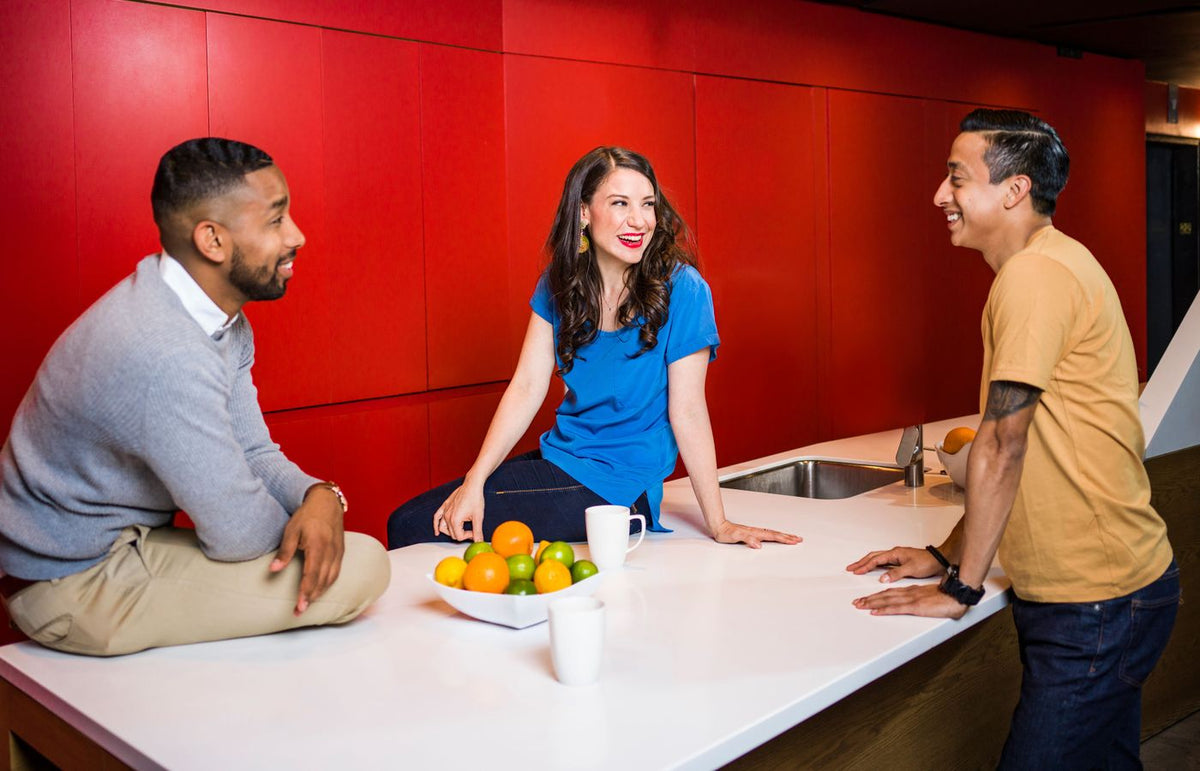 Three adults enjoy a friendly conversation in a modern kitchen with bold red decor.