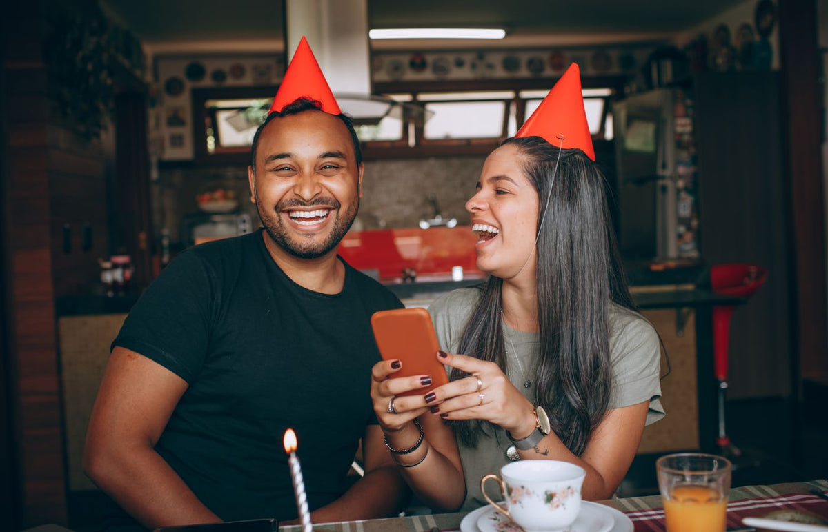 Two friends laughing and enjoying a birthday celebration indoors with party hats.