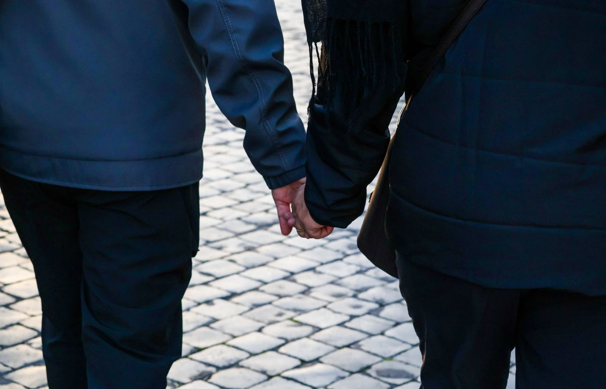 Back view of a couple holding hands walking on a cobblestone street.
