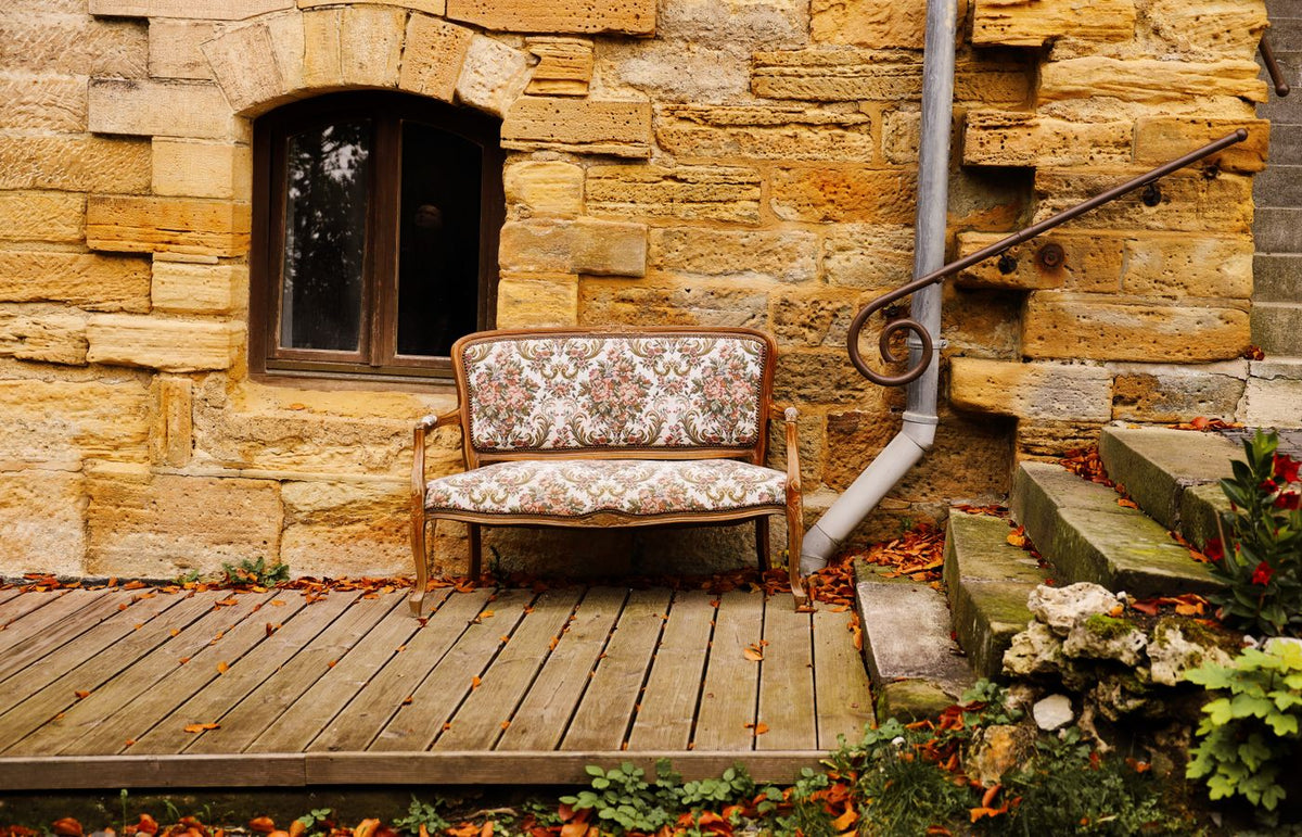 An inviting vintage bench placed by a rustic stone wall surrounded by autumn leaves.