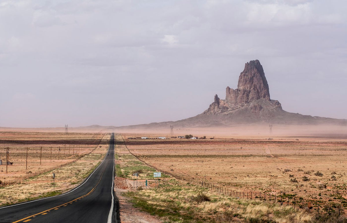 A long road stretches into a desert landscape with a towering butte in Monument Valley.