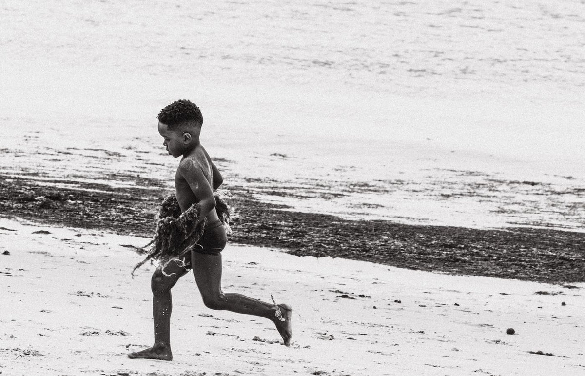 A young boy joyfully running on the beach in black and white photography.