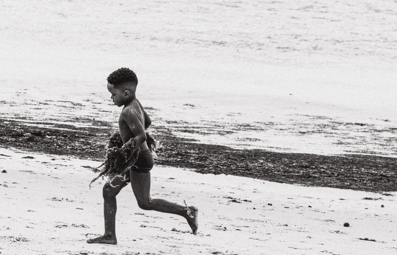A young boy joyfully running on the beach in black and white photography.