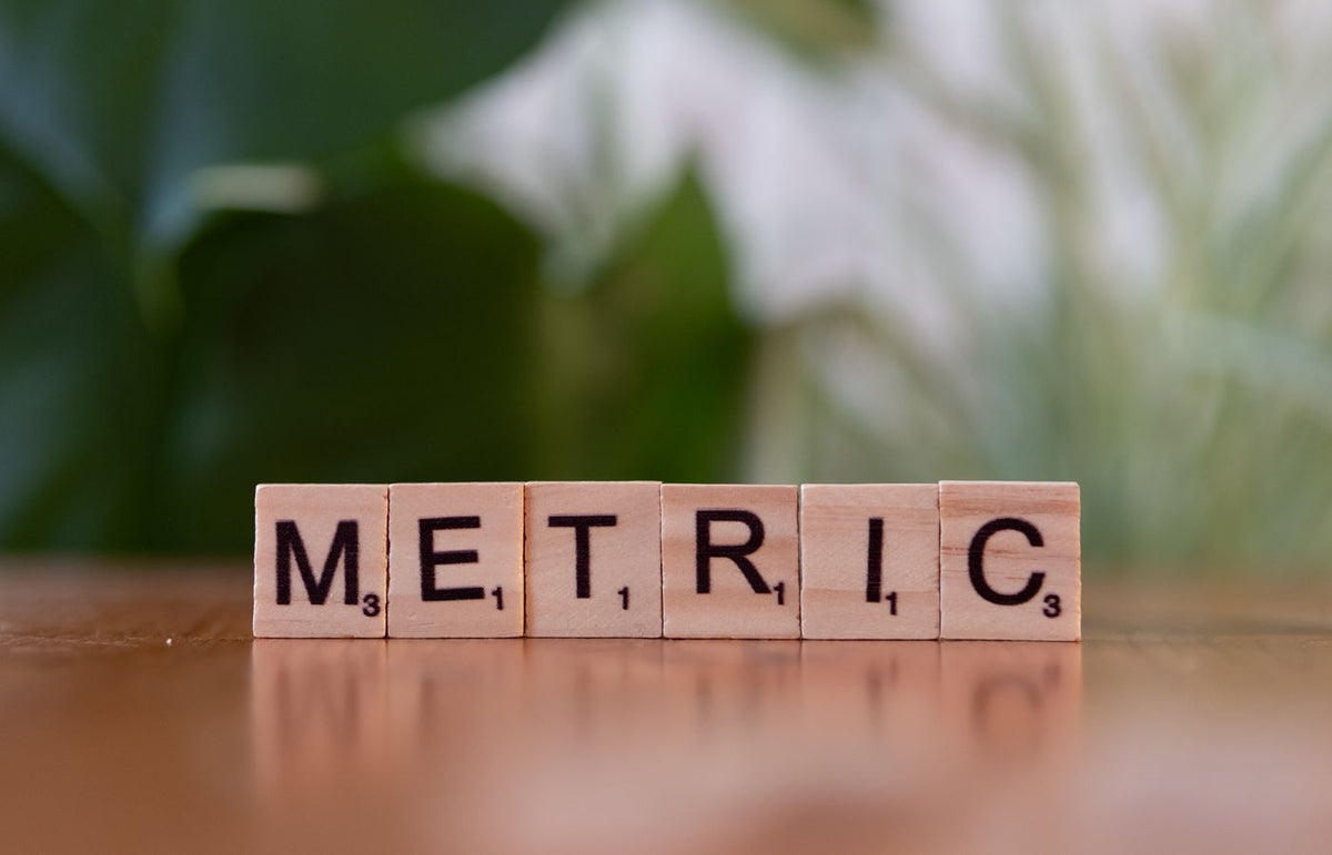 Close-up of wooden tiles spelling 'Metric' on a table, with a blurred green background.