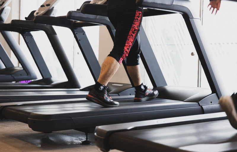A person walking on a treadmill in a modern gym setting, focusing on fitness.