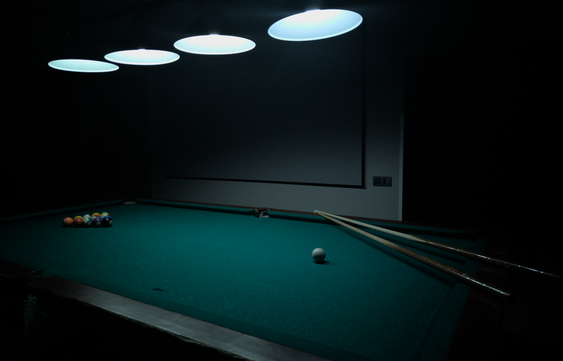 A billiards table under soft lighting with pool balls and cues ready for play.