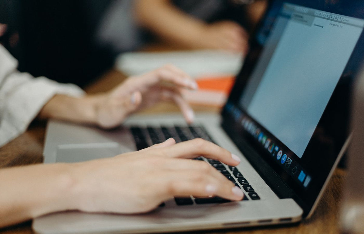 Person typing on a laptop in an office setting. Focus on hands and keyboard.