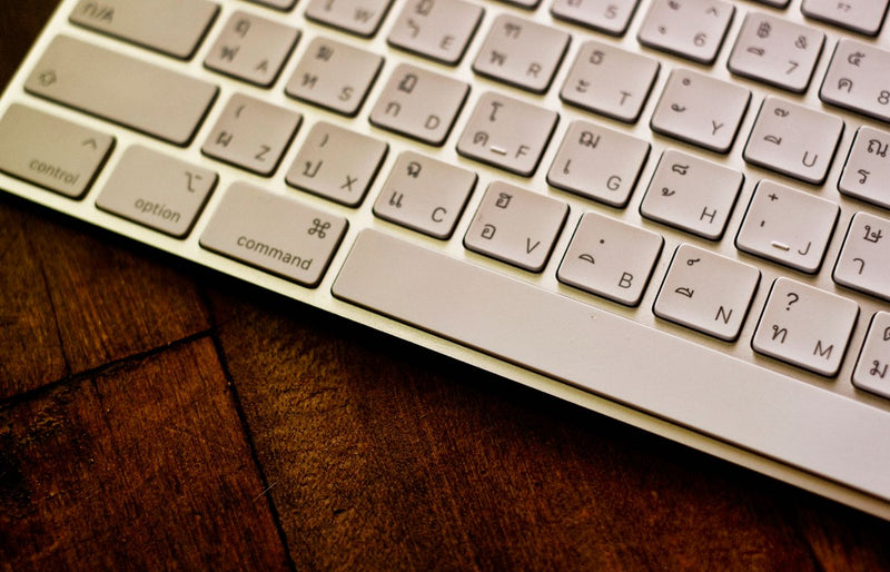 Close-up of a white Thai keyboard on a wooden desk, showing keys and textures.