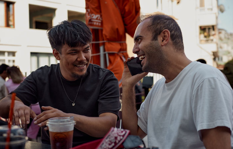 Two men smiling and chatting over drinks at an outdoor café.