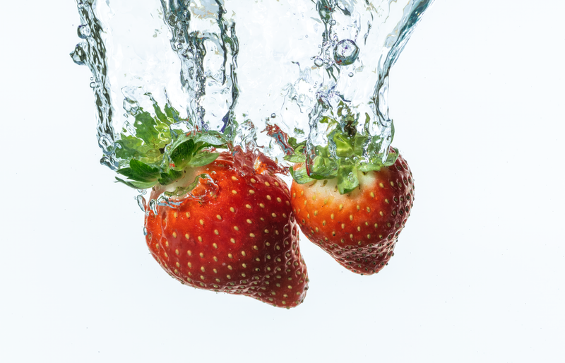 Two ripe strawberries splashing into clear water, isolated on white.