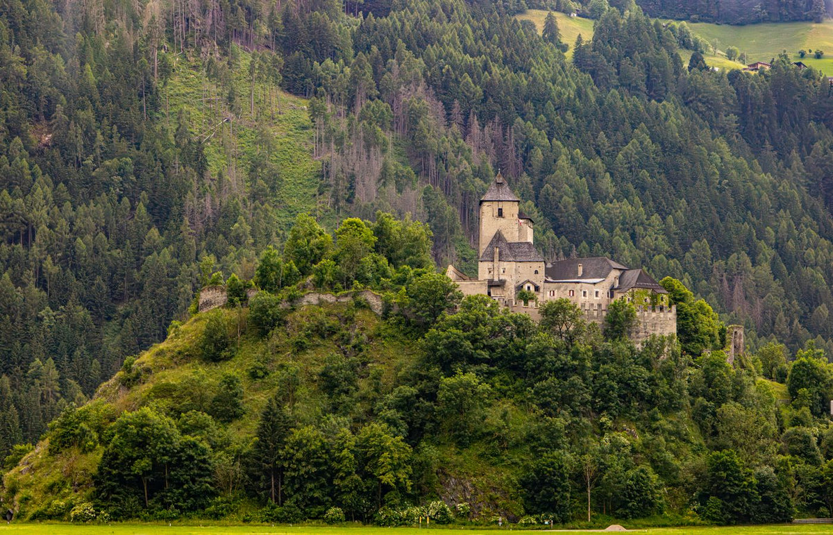 Serene view of a medieval castle nestled in the Austrian Alps surrounded by lush greenery.