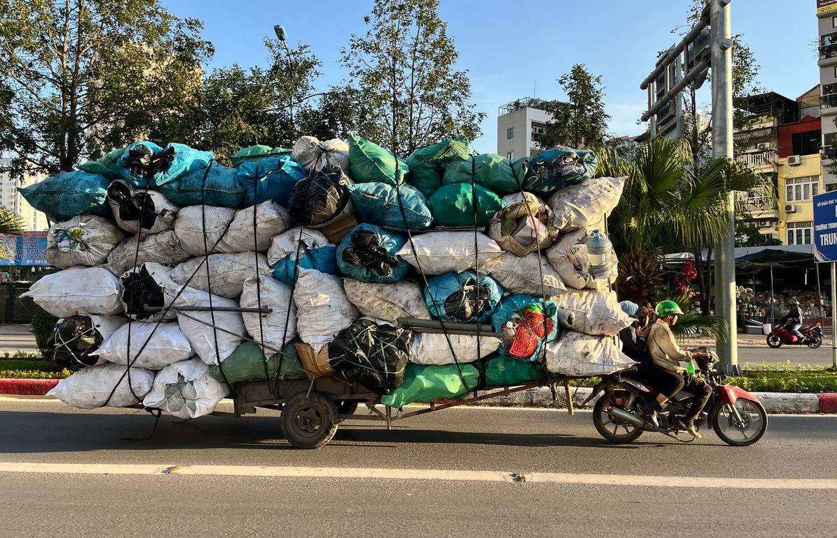 Motorcycle carries heavy load of bags on a street in Hanoi, creating an unusual scene.