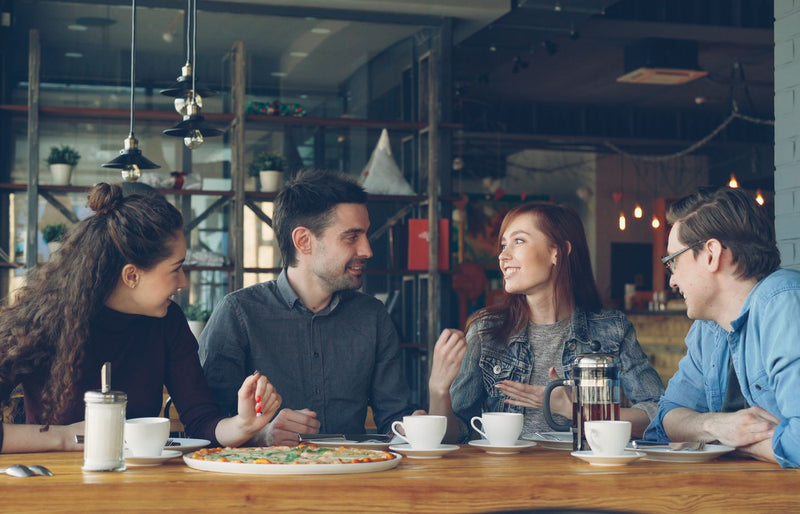 Group of friends laughing and talking over coffee in a stylish cafe setting.
