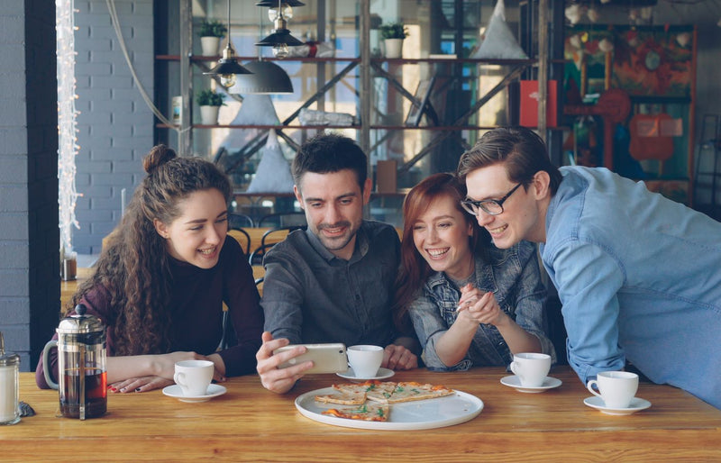 Four friends share a fun moment over coffee and pizza in a cozy cafe.