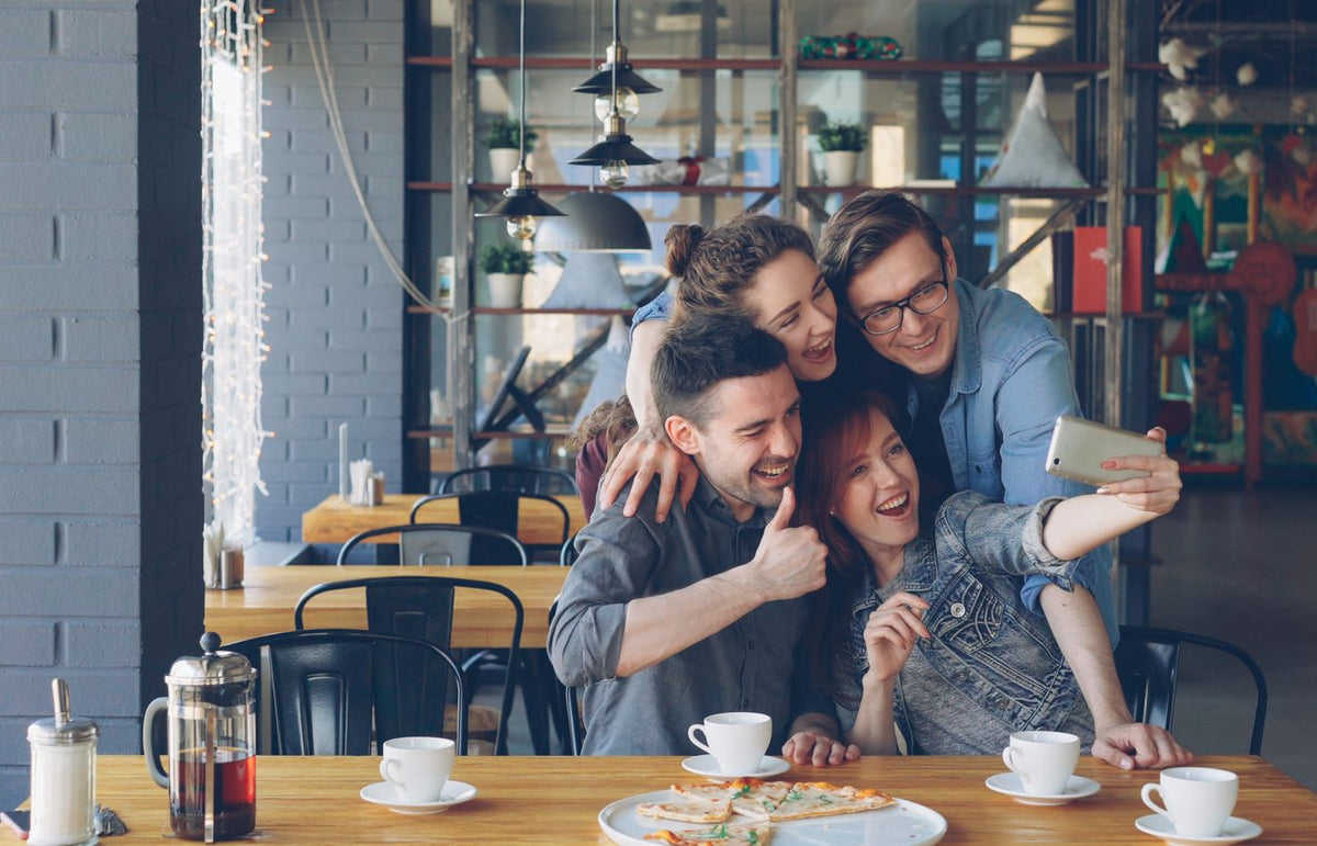 Group of friends taking a selfie at a café while enjoying coffee and pizza.