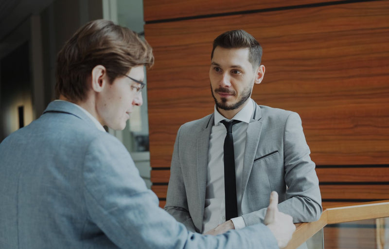 Two male professionals engaged in conversation in a modern office setting.