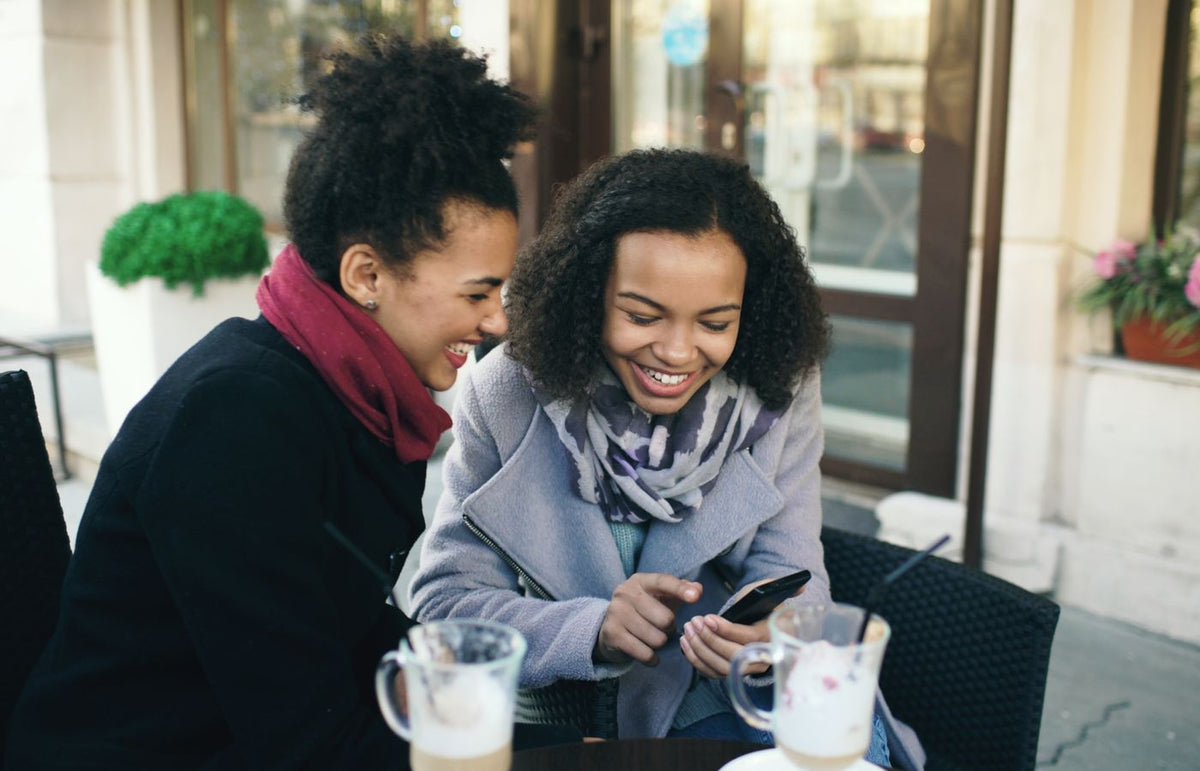 Two friends laughing over coffee at an outdoor cafe, sharing a joyful moment.