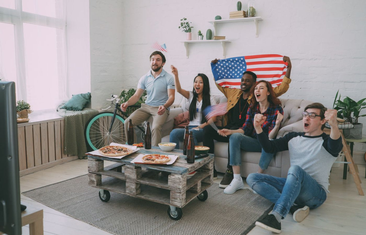 Group of diverse friends cheering for a sports event with American flags indoors.