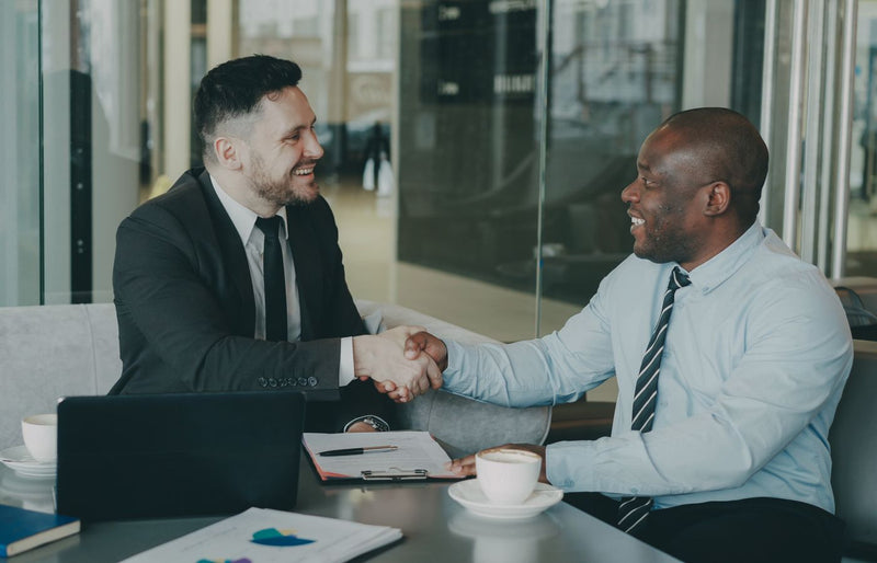 Two businessmen shaking hands over a deal at a modern office.