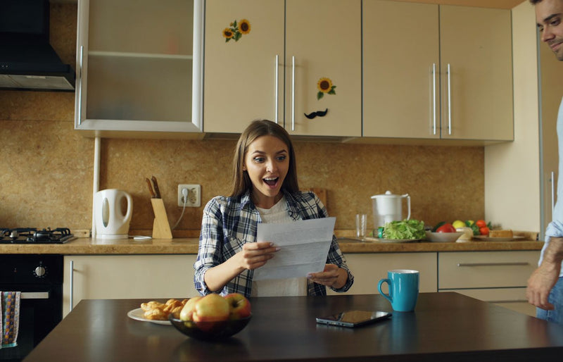 A woman joyfully reacts to good news in a cozy kitchen, embracing positivity and happiness.