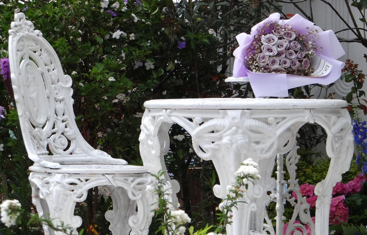 Elegant white garden furniture with a bouquet of roses under lush greenery, creating a serene outdoor setting.