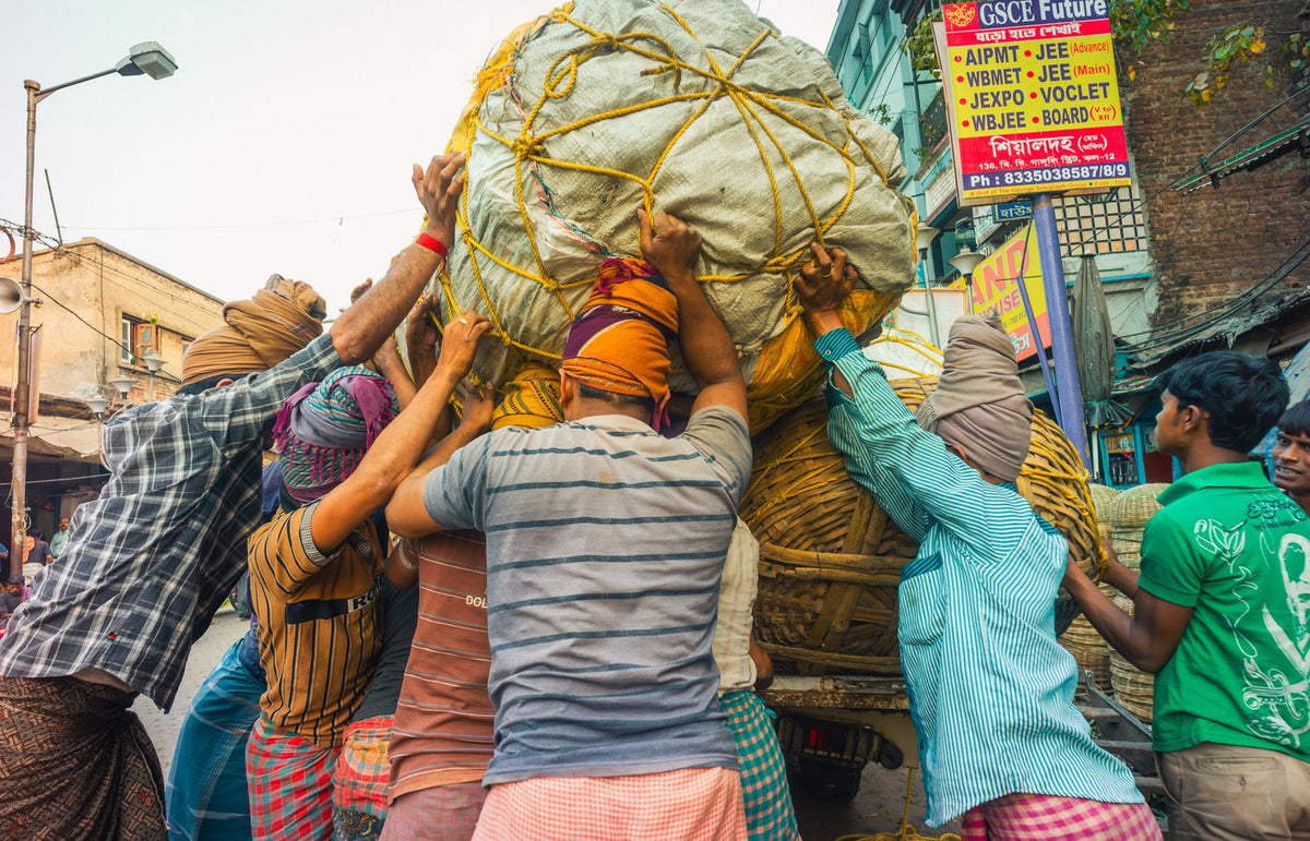 Group of laborers lifting heavy cargo in Kolkata market street, showcasing teamwork and local urban life.