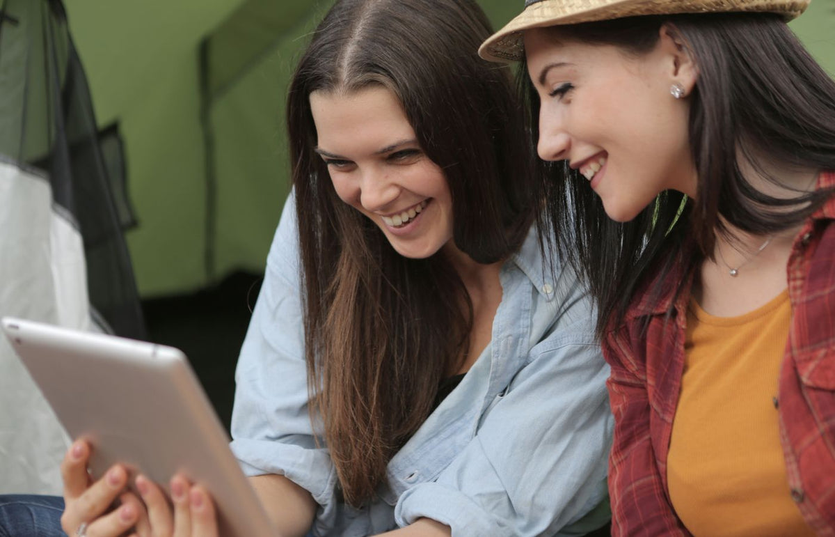 Two women laughing together while watching a tablet, showcasing friendship and happiness.