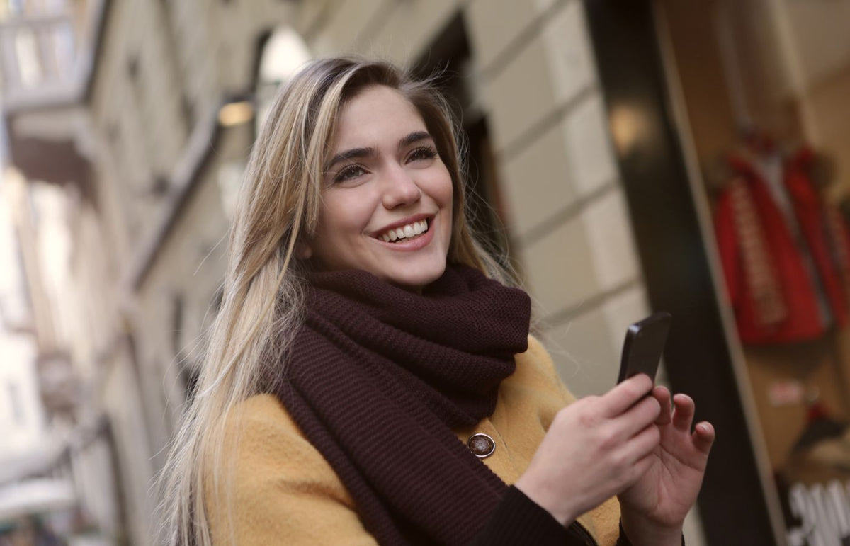 A happy woman using her smartphone while walking on a city street.