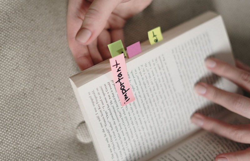 Hands holding a book with colorful sticky notes marking important pages.