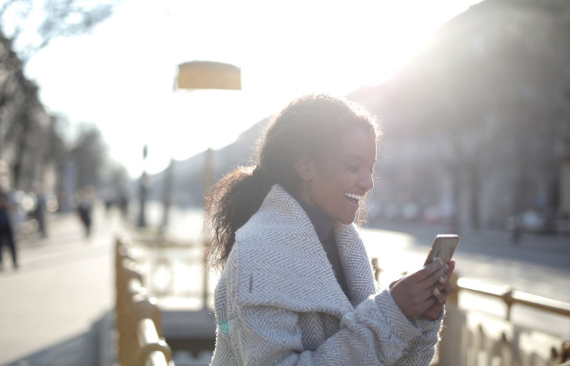 Smiling woman texting on phone in urban setting with winter backlight.