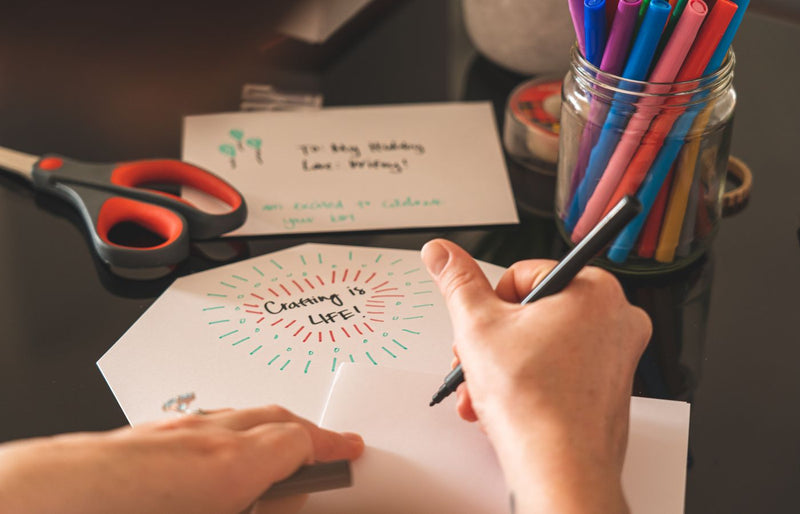 A creative workspace featuring colorful markers, scissors, and a handwritten card reading 'Crafting is Life!'.