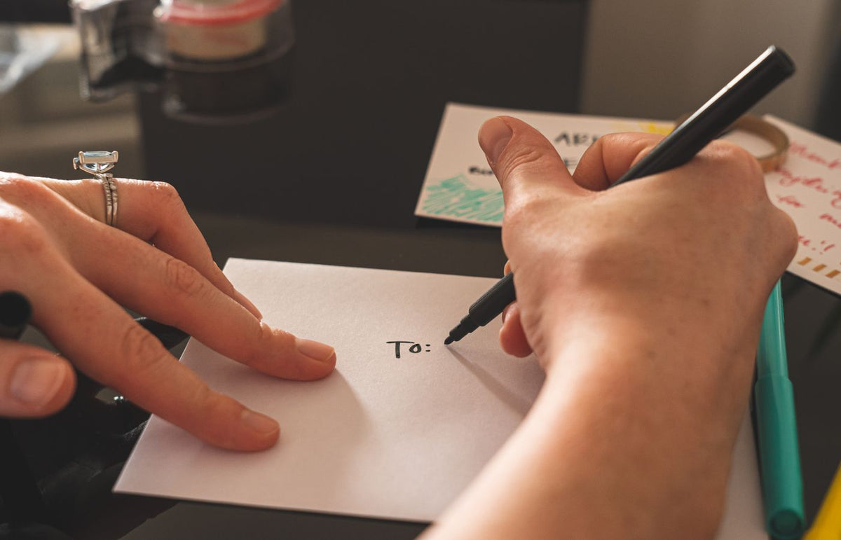 Hands writing on an envelope with marker, emphasizing handwritten correspondence.